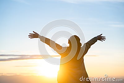 Woman standing alone with arms raised up during beautiful sunrise at the morning. Stock Photo