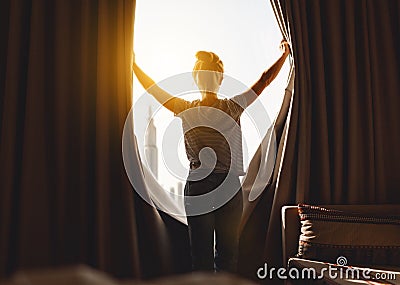 Happy woman stretches and opens curtains at window in morning Stock Photo