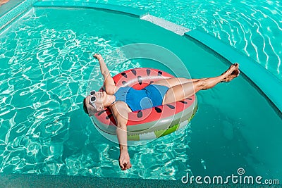 Happy woman in a swimsuit and sunglasses floating on an inflatable ring in the form of a watermelon, in the pool during Stock Photo