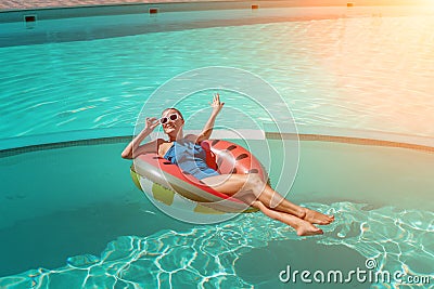Happy woman in a swimsuit and sunglasses floating on an inflatable ring in the form of a watermelon, in the pool during Stock Photo