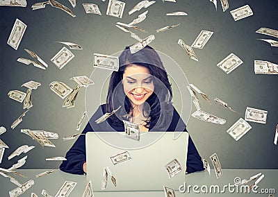 Happy woman using a laptop building online business under dollar bills falling down. Stock Photo