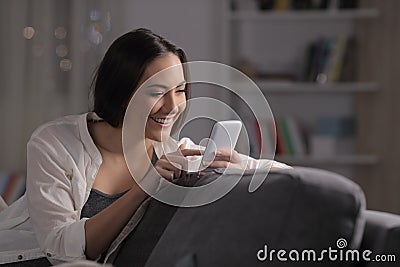 Happy woman using phone in the night on a couch Stock Photo