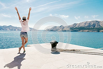 Happy woman on vacation standing by the sea. Arms raised. Carefree young female enjoy vacation. Stock Photo