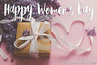 Happy women`s day floral greeting card. Handwritten greetings on lilac flowers and gift box on pink paper. International women`s Stock Photo