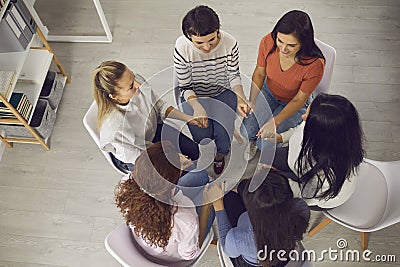 Happy women sitting in circle and holding hands in session with coach or in group therapy Stock Photo