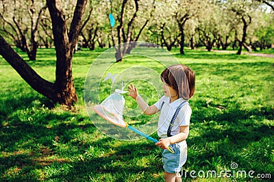 Happy 3 years old child boy catching butterflies with net on the walk in sunny garden or park Stock Photo