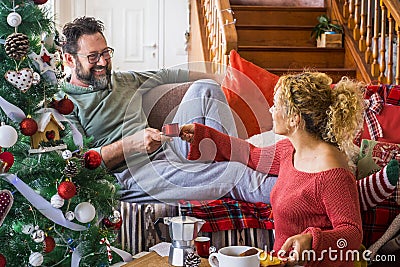 Happy young adult couple at home enjoying christmas morning in december taking coffee and breakfast together. Man smile to a woman Stock Photo