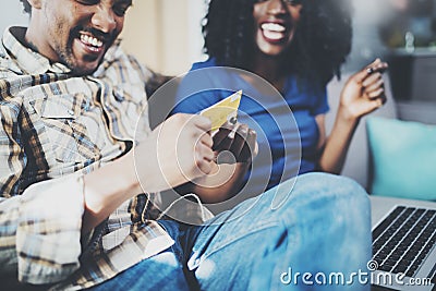 Happy young african american couple sitting on sofa at home and shopping online through mobile computer by credit card Stock Photo