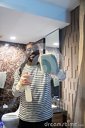 Happy young African American man cleaning the glass in the apartment. Cleaning maintain cleanliness in with towel and Stock Photo