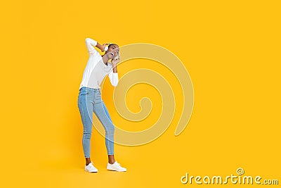 Happy young African American woman listening to music on headphones on yellow studio background with copy space Stock Photo