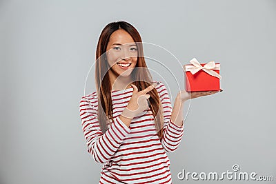 Happy young asian lady standing isolated holding gift and pointing. Stock Photo