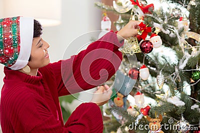 Happy young asian woman smiling hanging decorating ornament on Christmas tree in the living room at home. Stock Photo