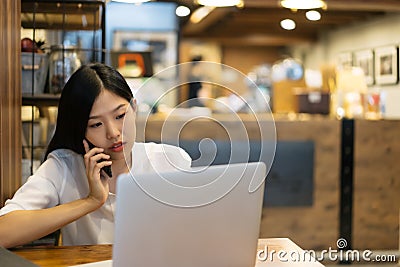 Happy young Asian woman using phone and working with a laptop in the coffee shop cafe office. Stock Photo