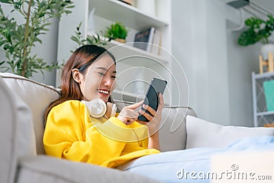 Happy young asian woman wearing headset and relaxing on comfortable couch at home Stock Photo