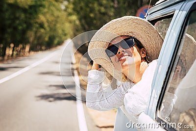 Happy young beautiful caucasian people female enjoy the sun outside the window of blue old vehicle - long road in background for Stock Photo