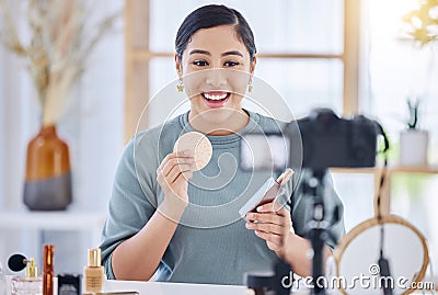 Happy young beauty blogger holding up a beauty product and sponge while doing a make-up tutorial and recording with her Stock Photo