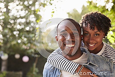 Happy young black couple piggyback in garden, look to camera Stock Photo