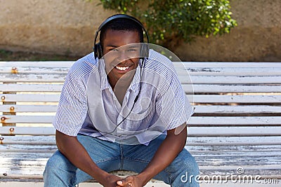 Happy young black man sitting on park bench with headphones Stock Photo