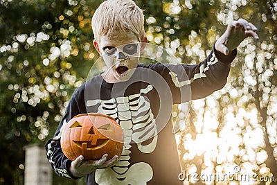 Happy young blond hair boy with skeleton costume holding jack o lantern. Halloween. Trick or treat. Outdoors portrait Stock Photo