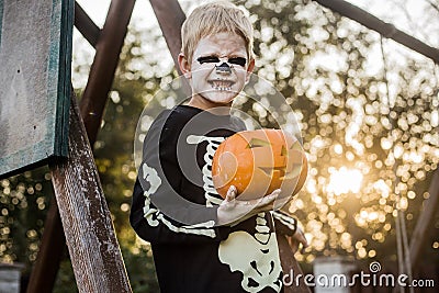 Happy young blond hair boy with skeleton costume holding jack o lantern. Halloween. Trick or treat. Outdoors portrait Stock Photo