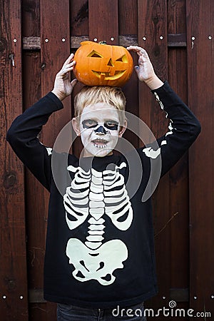 Happy young blond hair boy with skeleton costume holding jack o lantern. Halloween. Trick or treat. Outdoors portrait over wooden Stock Photo