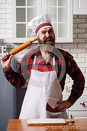 Happy young blond man in an apron in the kitchen with rolling pin in his hands, dancing having fun. Cooking Love. Stock Photo