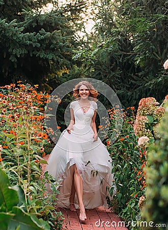 Happy young blonde girl in an elegant amazing long white wedding light dress with a long train, walking in a wonderful Stock Photo