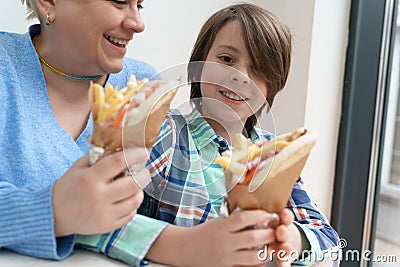 Happy young boy enjoying Greek gyro sandwich together with his mother. Cheerful Ukrainian family eating traditional gyros pita Stock Photo