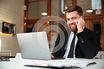 Happy young businessman in black suit talking on mobile phone, l Stock Photo