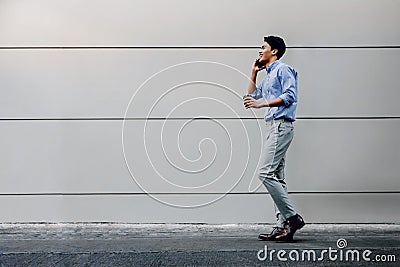 Happy Young Businessman in Casual wear Using Mobile Phone while Walking by the Urban Building Wall. Lifestyle of Modern People. Stock Photo