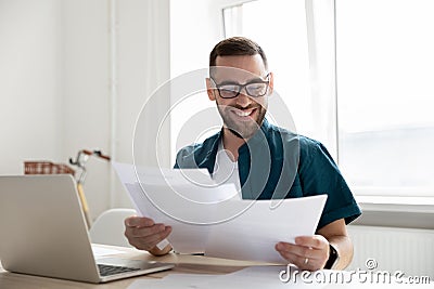 Happy young businessman in glasses looking through paper documents. Stock Photo