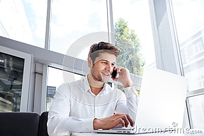 Happy young businessman talking on cell phone and using laptop Stock Photo