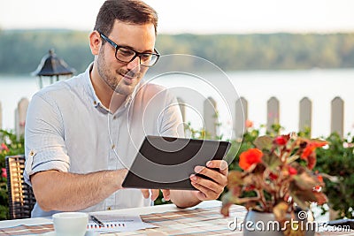 Young freelancer drinking coffee in riverside cafe and browsing internet on a tablet Stock Photo