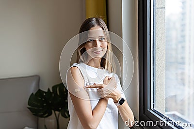Happy young caucasian woman with blonde hair in white t-shirt showing patch on arm, feeling good after anti coronavirus Stock Photo