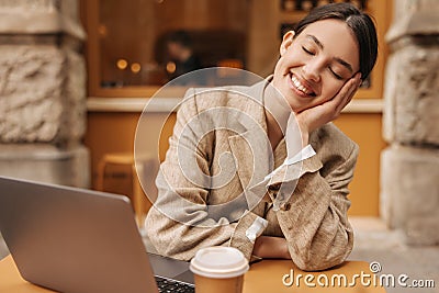Happy young caucasian woman closing eyes smiles with teeth lying on arm sitting in cafe. Editorial Stock Photo