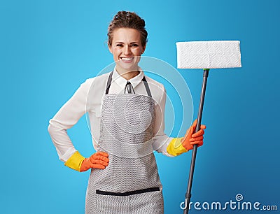Happy young cleaning lady in apron with mop on blue Stock Photo
