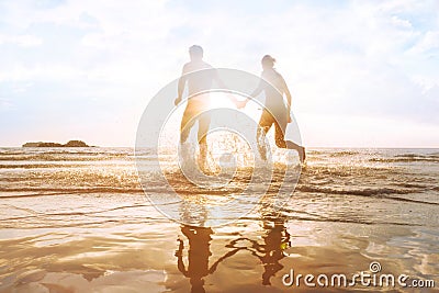 Happy young couple having fun on the beach at sunset, water splash Stock Photo