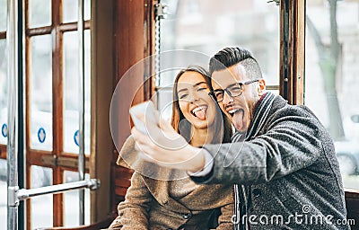 Happy young couple taking photos using mobile smart phone camera inside bus - Travel lovers making a self portrait Stock Photo