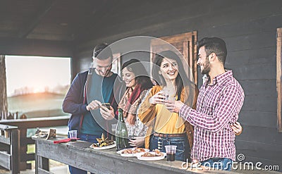 Happy young couples toasting red wine and eating barbecue in backyard wooden house - Cheerful people having fun at sunset in Stock Photo