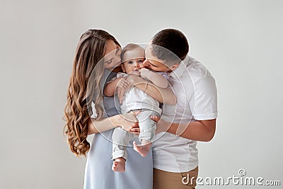 Happy young family. Beautiful Mother and father kissing their baby. Portrait of Mom, dad and smiling child on hands Stock Photo