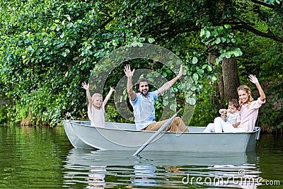 happy young family with raised hands riding boat on lake Stock Photo