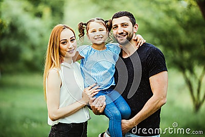 Happy young family spending time together in green nature. wife with husbend and daughter. Mother and father holding daughter in p Stock Photo