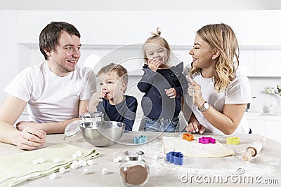 Happy young family with two small children cheerfully prepares dough cookies in the kitchen. Love and tenderness in a relationship Stock Photo