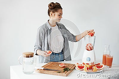 Happy young girl blending healthy detox fresh grapefruit smoothie over white wall. Stock Photo