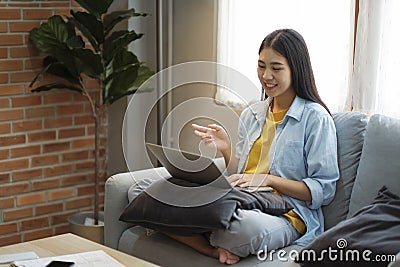 Happy young girl having video call on laptop while sitting on couch at home. Stock Photo