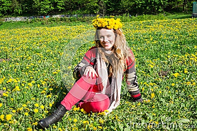 Happy young girl sitting in the park on a field of grass and dandelions with a bouquet of dandelions on his head and smiling Stock Photo