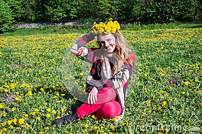 Happy young girl sitting in the park on a field of grass and dandelions with a bouquet of dandelions on his head and smiling Stock Photo