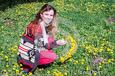 Happy young girl sitting in the park on a field of grass and dandelions and picking flowers to make a bouquet Stock Photo