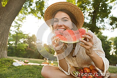 Happy young girl in summer hat having a picnic at the park, sitting on a grass Stock Photo