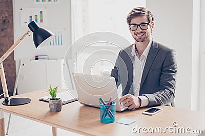 Happy young handsome businessman in glasses is sitting at desk in workplace, smiling and looking directly at camera Stock Photo